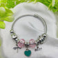 Silver bracelet with pink and teal charms on a white fabric background with green leaves.