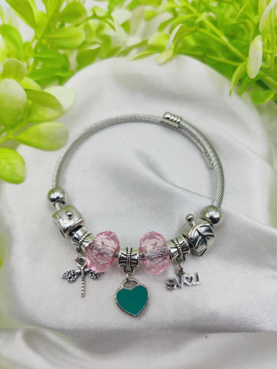 Silver bracelet with pink and teal charms on a white fabric background with green leaves.